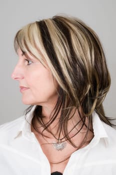 Head portrait of a mature blonde woman with dark streaks looking to the side with head and eyes