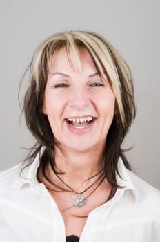 Head portrait of mature blonde woman with dark streaks looking at camera smiling and frontally
