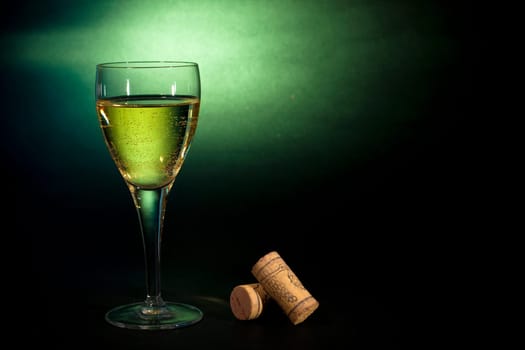 White wine in a glass, on black-green background. Art background