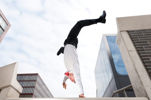 Young businessman in handstand in front of sky and house front
