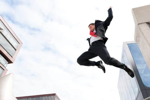 Young businessman jumping in front of sky and house front