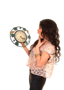 Pretty Asian woman in tights and beige blouse with long curly hair standing with a clock in her hand realizing it is to late, over white.