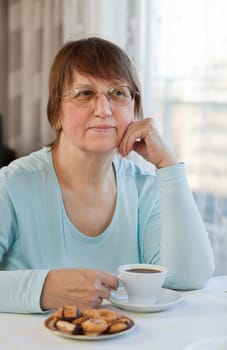 Elderly woman enjoying a cup of coffee with cookies at home