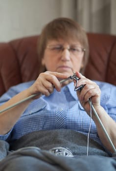 Elder woman doing knitting at home, focus on hands and needles