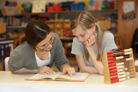Teacher and student sitting at school desk with a textbook on learning together