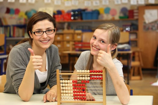 Teacher and student sitting at a desk at school or in the classroom and both show up the thumb.