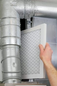 A male arm and hand seen replacing disposable air filter in home central air furnace.