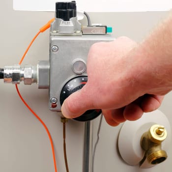 Hand of a man turning down household gas water heater temperature.