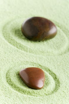 Brown stones in balance in a circle on green sand