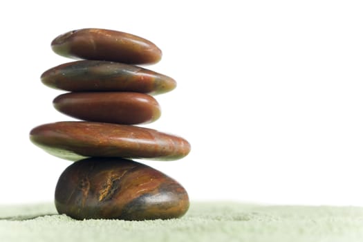 Brown stones in balance on green sand against white background