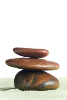 Brown stones in balance on green sand against white background