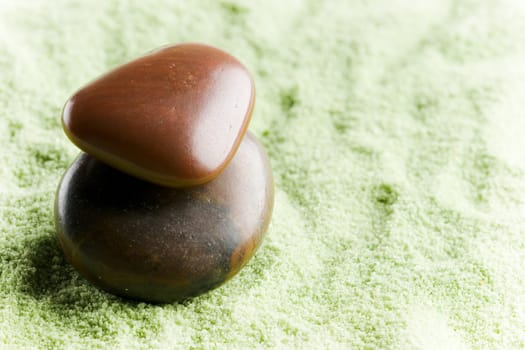 Brown stones in balance on green sand