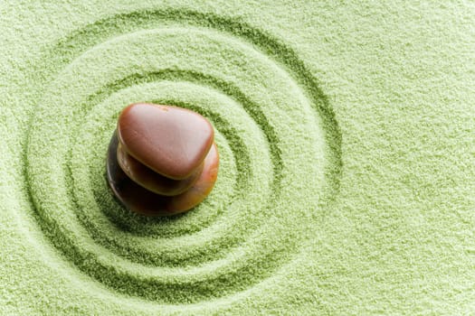 Brown stones in balance in a circle on green sand