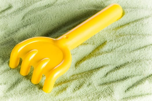Yellow toy rake isolated on green sand