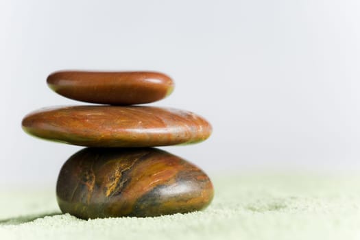 Brown stones in balance on green sand against white background