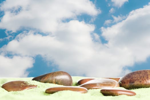Brown stones messed up on green sand against blue sky with clouds
