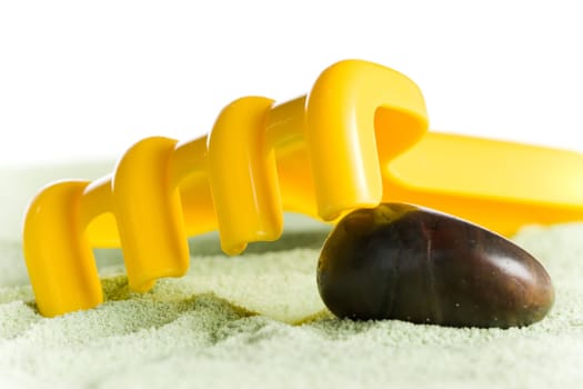 Yellow toy rake with brown stone on green sand