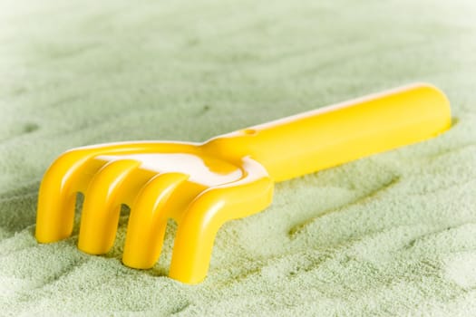Yellow toy rake isolated on green sand