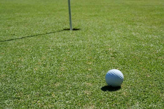 A Golf Ball on green near hole with flag pole