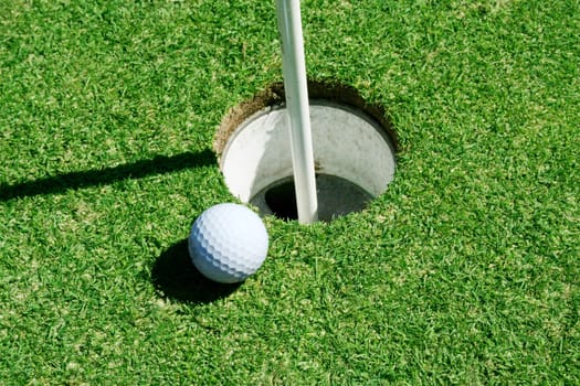 A Golf Ball on green near hole with flag pole