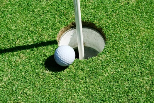 A Golf Ball on green near hole with flag pole