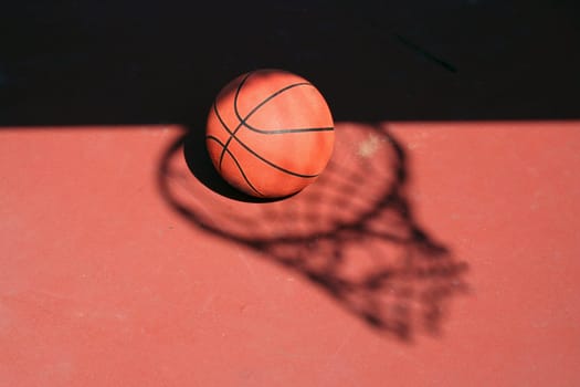 A Basketball and net shadow on a red court