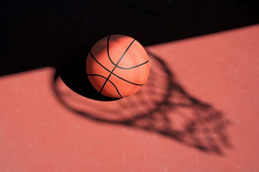 A Basketball and net shadow on a red court