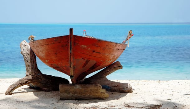 A Small Red Wooden Boat On A Sunny Ocean Beach