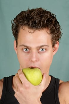 Young man biting a granny smith apple over a green background. Concept for healthy eating.