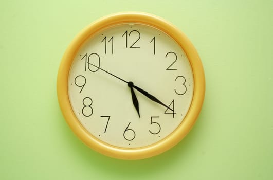 Yellow wall clock on the green background