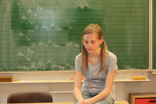 Sad blonde girl at school in front of a blackboard with her head bowed