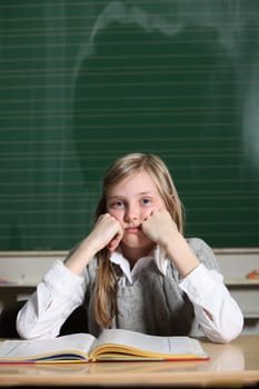 A child sits with a book in front of a blackboard at school and thinks