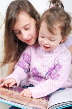 Sisters sitting in living room reading book