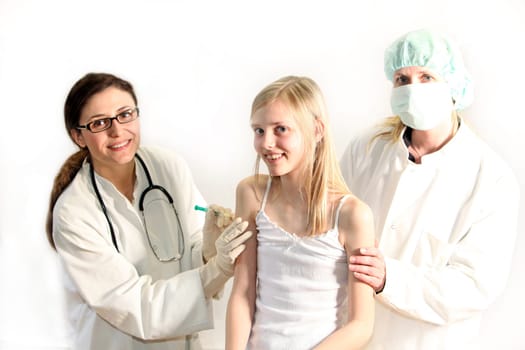 A young girl receives an injection from a doctor. A nurse with a face mask is right