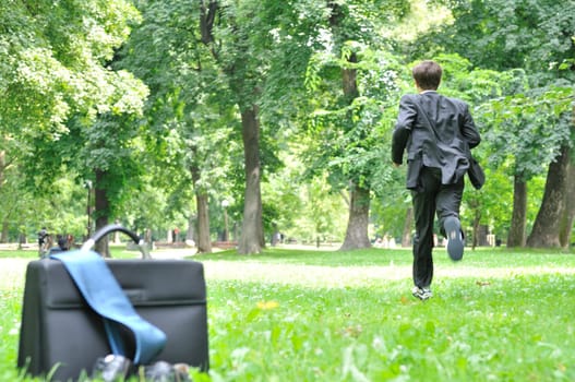 Escape from civilization concept - business man running in park away from bag, shoes and tie