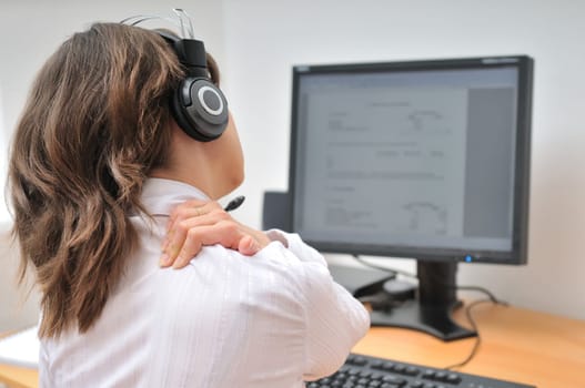 Young business person with neck pain. Focus on hand on neck with blurred monitor on table in background.