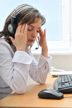 Young tired call center employee with headache sitting at computer on workplace