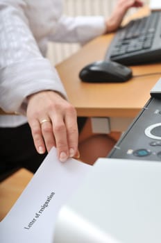 Hand of business woman reching paper (letter of resignation written on) from printer on workplace