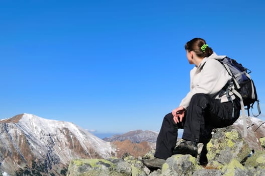 Hiker relaxing on rocky hill with clear blue sky