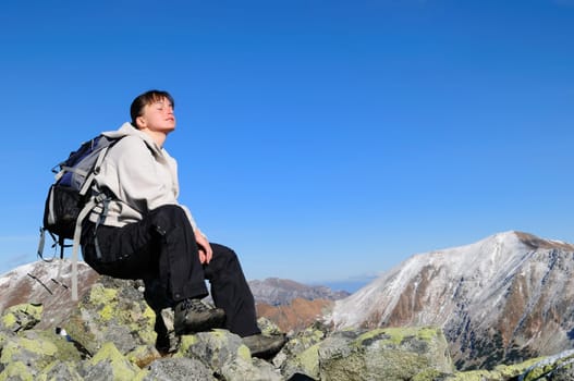 Hiker relaxing on rocky hill with clear blue sky with face turned to sun