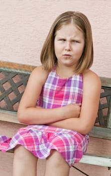 Outdoors portrait of small cute girl sitting on bench with angry expression