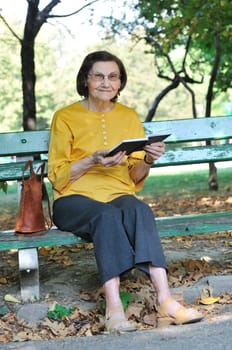 Senior woman sitting on bench reading book outdoors in park