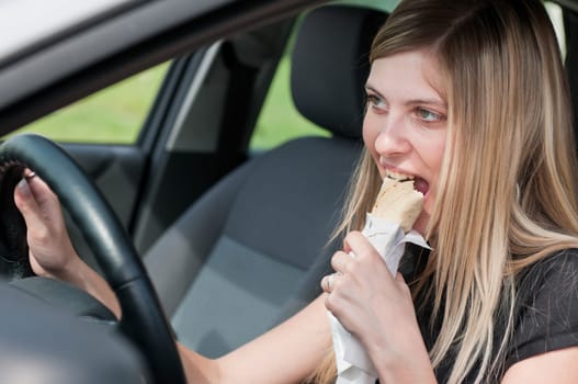 Young beautiful smiling woman driving car and eating fast food - portrait through side window