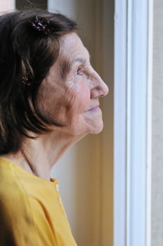Solitude concept  - sad 80s senior woman looking through window at home