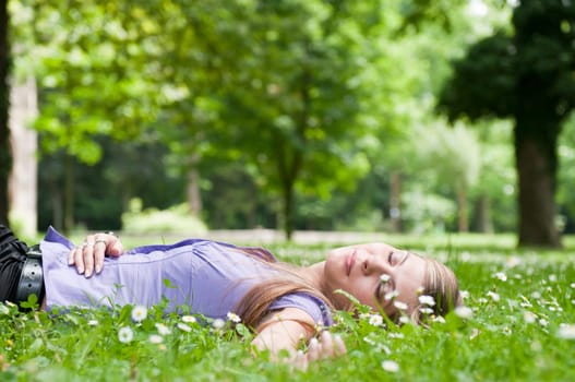 Relaxed young person (teenage girl) lying in grass and flowers with stretched hand - closed eyes