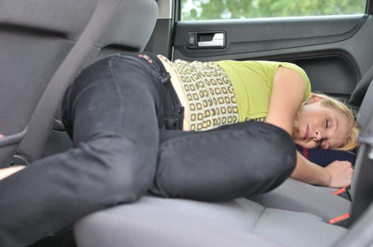 Young beautiful blond woman sleeps in car on back seat - lifestyle portrait