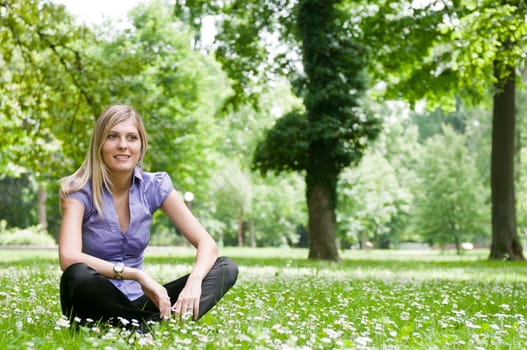 Young smiling woman siting in grass with flowers - outdoors scene