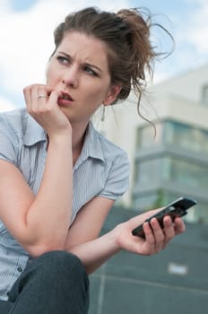 Young worried woman with unhappy expression holding mobile phone - outdoors in urban setting