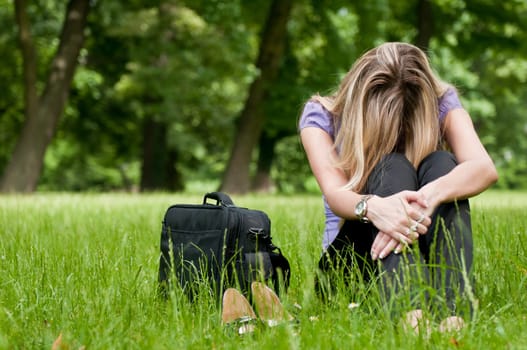 Young depressed business woman siting in grass - notebook bag and shoes lying next