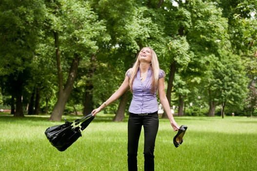Young woman enjoying life outdoors - spinning around and holding bag and shoes